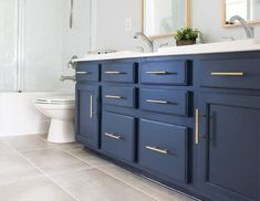 a white toilet sitting next to a blue vanity in a bathroom under a mirror on top of a wooden cabinet