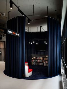 the interior of a library with black curtains and white chairs, bookshelves, and a red chair