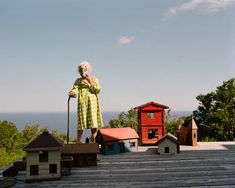 an old woman standing on top of a wooden deck next to some houses and trees