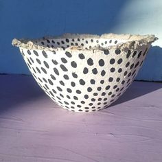 a white and black spotted bowl sitting on top of a table next to a blue wall