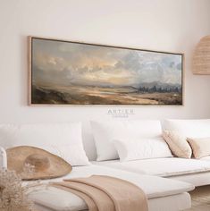 a painting hanging on the wall above a white couch in a living room with pillows