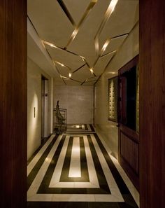 a hallway with black and white striped flooring next to a tall wooden door that has lights hanging from the ceiling