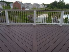 a wooden deck with white railings overlooking a lake and houses in the back ground