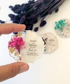 a person holding up a flower shaped business card next to some purple and green flowers