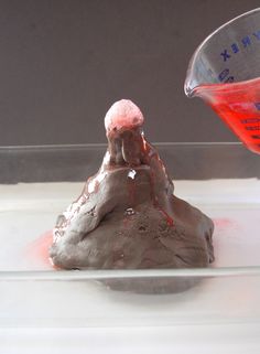 someone is pouring red liquid into a small rock shaped like a volcano with lava on top