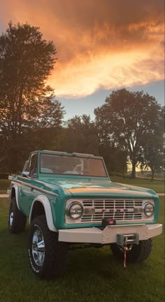 an old pickup truck parked in the grass under a cloudy sky with trees behind it