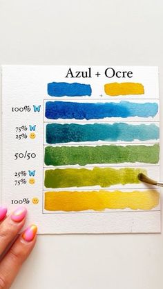 a hand holding a paintbrush over a watercolor swatch with the words azul + ocre on it