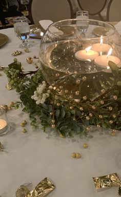 candles are lit in a bowl with greenery and gold foil wrap around the edges