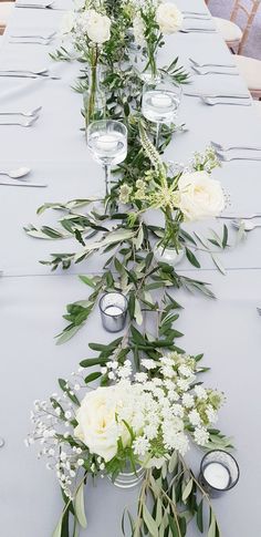 a long table with white flowers and greenery in vases on the top row