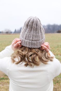 a woman standing in a field with her back to the camera wearing a knitted hat