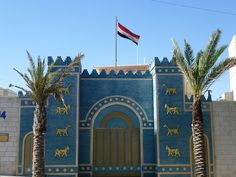 a blue building with two palm trees in front of it and a flag on top