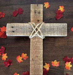 a wooden cross surrounded by fall leaves on a wood table with red, orange and yellow leaves scattered around it