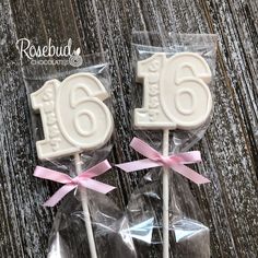 two white cake pops with pink bows on them and the number sixteen on each stick