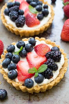 some pies with fruit on top of them sitting on a black table and one has blueberries, raspberries, and strawberries in the middle