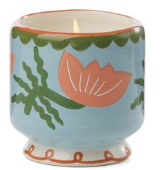 a ceramic candle holder with an orange flower and green leaves on blue, white background