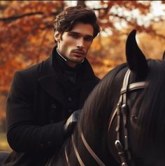 a man riding on the back of a black horse in front of trees with orange leaves