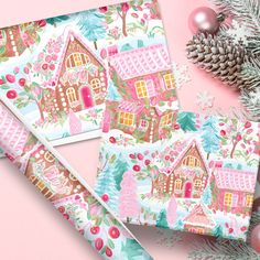 three christmas wrappings on top of a pink surface next to pine cones and ornaments