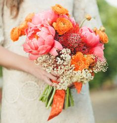 a woman holding a bouquet of orange and pink flowers on her wedding day in an outdoor setting