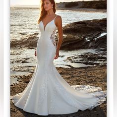 a woman in a white wedding dress standing on the rocks near the ocean at sunset