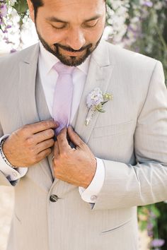 a man in a gray suit adjusts his pink tie and flower boutonniere