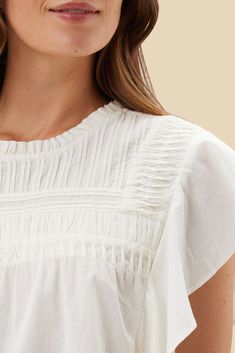 Timeless and feminine. The Aida Blouse, crafted in organic cotton with beautiful pin tucking and ruffle details, exudes a subtle romantic charm. Short-sleeved shirt with neck ruffle, pleat, and shirring detail at yoke, cascading ruffle sleeve, and loop and button closure with slit at back 100% Organic Cotton Cambric 43"" in Length Ethically Made in India Organic Cotton Clothing, Sustainable Brand, Cotton Blouse, Neck Ruffle, Pin Tucks, Cotton Blouses, Ivory Color, Short Sleeve Blouse, Cotton Shorts