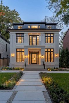 a large white house with lots of windows and lights on the front door is lit up at night