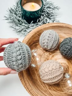 three crocheted balls sitting on top of a wooden plate next to a candle