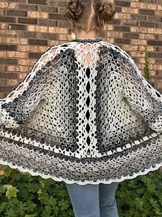 a woman standing in front of a brick wall wearing a crocheted shawl