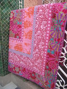 there is a pink and green quilt hanging on the wall next to each other in front of a building