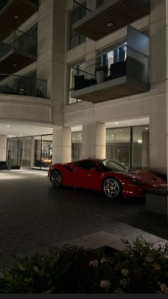 a red sports car is parked in front of a building at night with its lights on