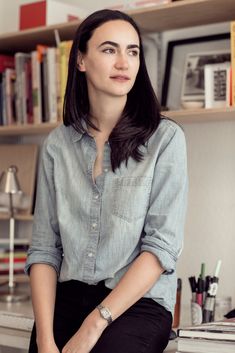 a woman sitting on top of a desk next to a book shelf