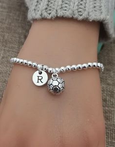 a person wearing a silver bracelet with a soccer ball charm