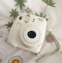 a white camera sitting on top of a bed next to a flowered sheet and pillow