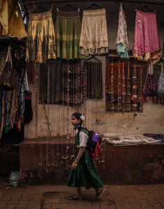 a woman walking down the street in front of some clothes hanging on a rack and other items