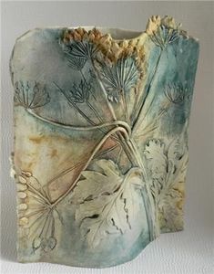 a ceramic vase with flowers and leaves on the outside, sitting on a white surface