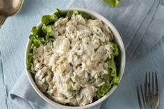 a bowl of chicken salad with lettuce on a blue wooden table next to silverware