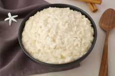 a bowl filled with rice next to two wooden spoons on top of a table