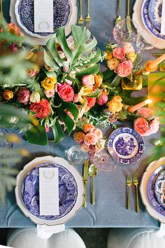 the table is set with blue and white plates, silverware, and colorful flowers