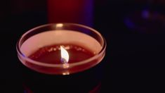 a lit candle sitting on top of a table next to a red glass cup with liquid in it