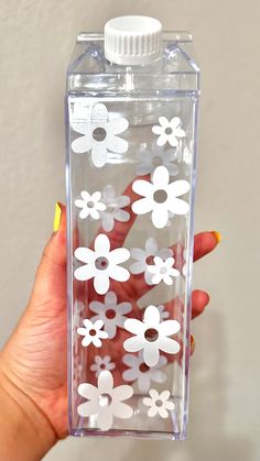 a person holding up a clear bottle with white flowers on the front and bottom half