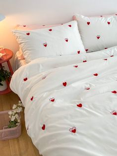 a bed with white sheets and red hearts on the comforter is next to a pink table