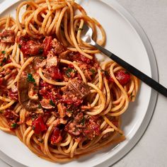 a white plate topped with pasta and meat covered in tomato sauce next to a fork