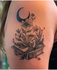 a woman's thigh with an open book and flowers on it, next to the moon