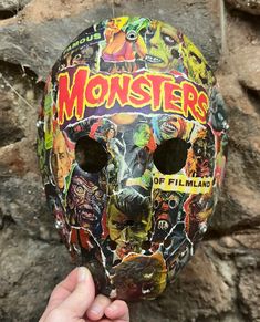 a person holding up a mask that has been painted with monsters and other things on it