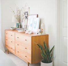 an image of a dresser with pictures and plants on it's top shelf next to a door