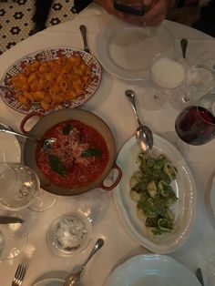 a table filled with plates and bowls of food next to wine glasses on top of it