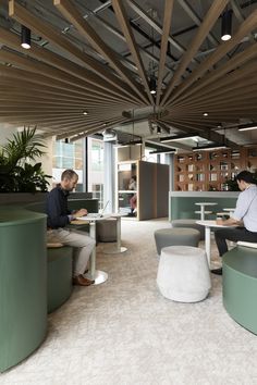 two people are sitting at tables in an office with green chairs and white stools