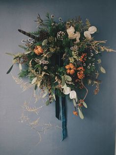 an arrangement of flowers and foliage is hanging on the wall in front of a blue wall