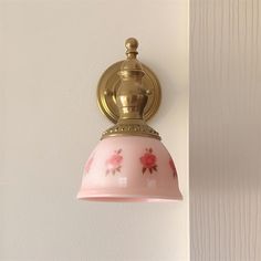 a pink and gold light hanging from the side of a wall next to a white wall