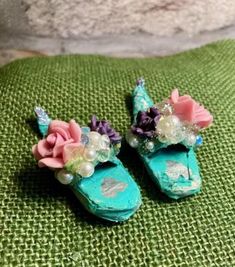 two miniature shoes with flowers on them sitting on a green surface next to a pillow